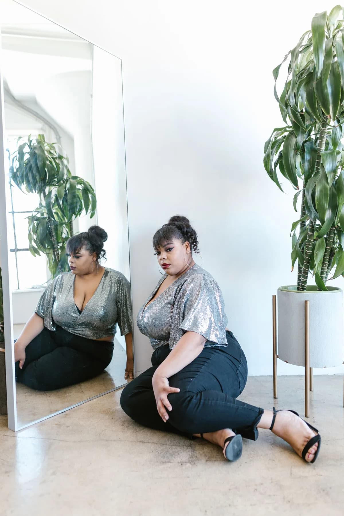 Plus-size woman in silver blouse and black trousers beside a mirror